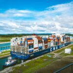 A vast cargo ship passes through the Panama Canal on a bright day, showcasing global trade.
