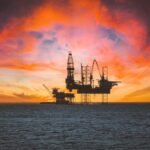 Offshore oil rig silhouetted against a vibrant sunset with dramatic clouds.