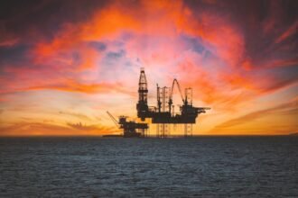 Offshore oil rig silhouetted against a vibrant sunset with dramatic clouds.