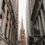 View of Trinity Church between skyscrapers on Broad Street, NYC, showcasing historic architecture.