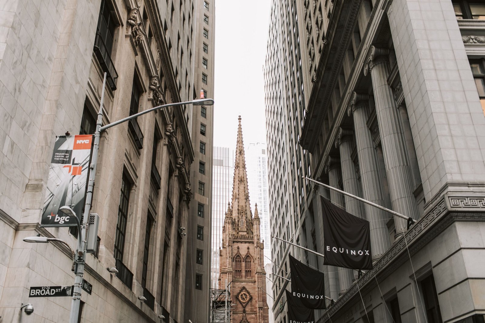 View of Trinity Church between skyscrapers on Broad Street, NYC, showcasing historic architecture.