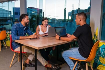 Three colleagues sitting at a table working on laptops in a vibrant, urban office space.