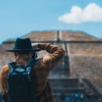 Man in black hat capturing Teotihuacán pyramid with camera and backpack.