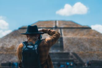 Man in black hat capturing Teotihuacán pyramid with camera and backpack.